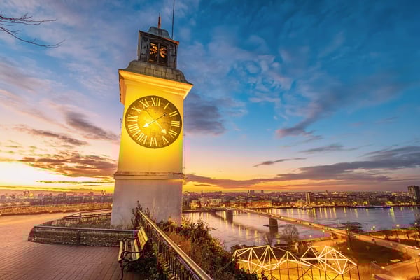 Beleuchteter Uhrturm auf Anhöhe mit Blick über Stadt und Brücken
