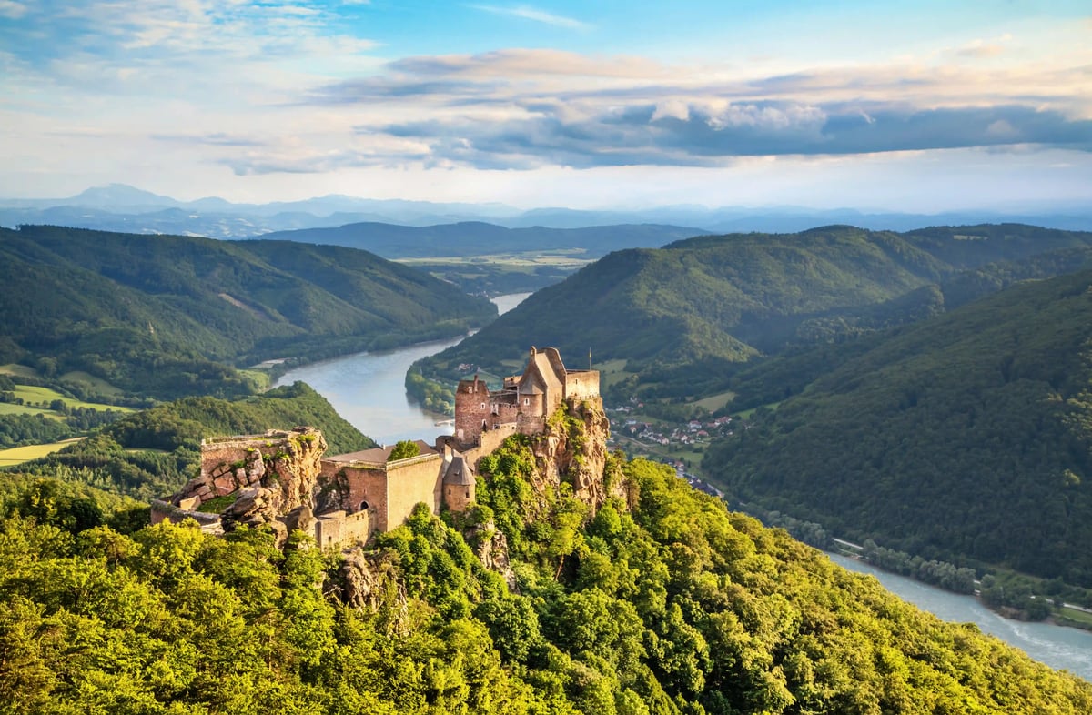Steinerne Burgruine thront auf Felsen über grünem Tal und Donau Landschaft