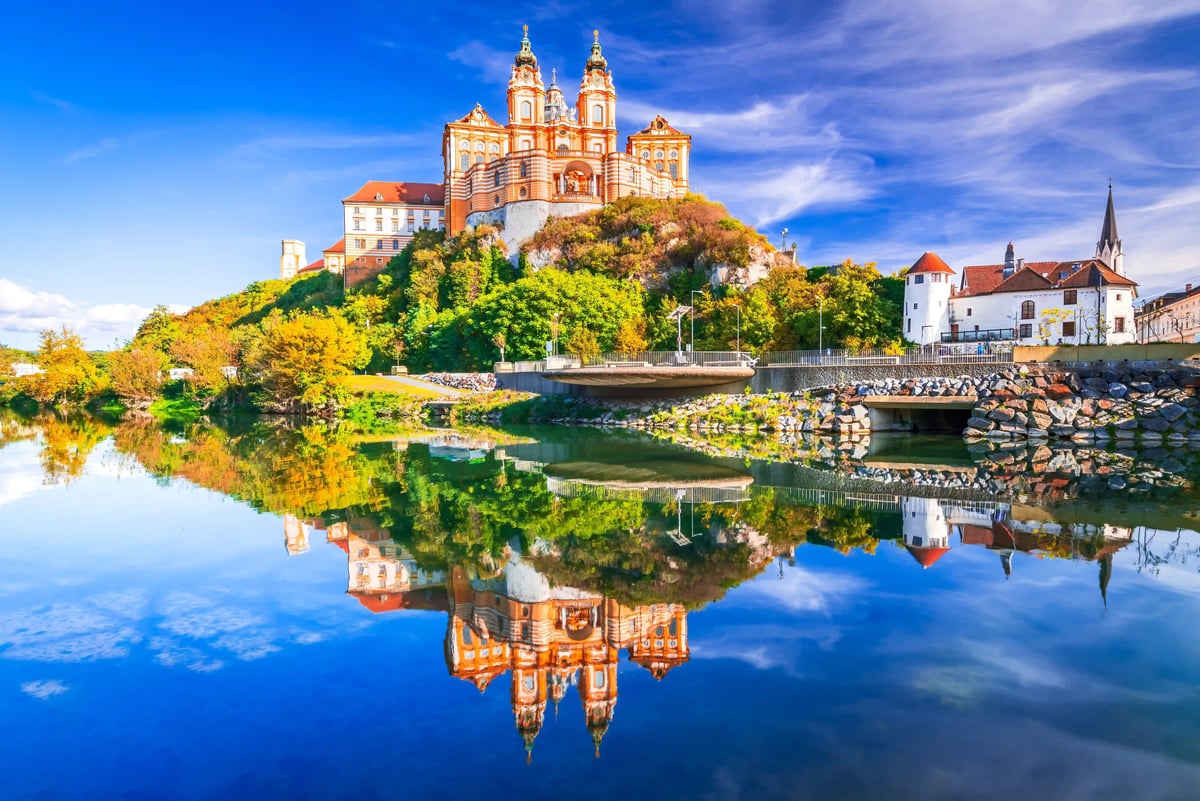 Barockes Stift auf Hügel spiegelt sich im ruhigen Wasser bei blauem Himmel