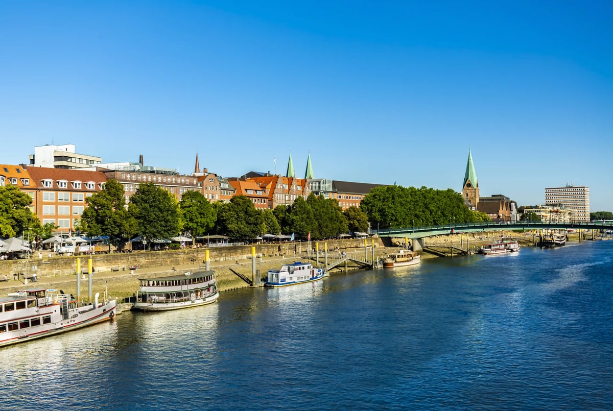 Uferpromenade an der Weser in Bremen mit Schiffen, Bruecke und Stadtsilhouette.