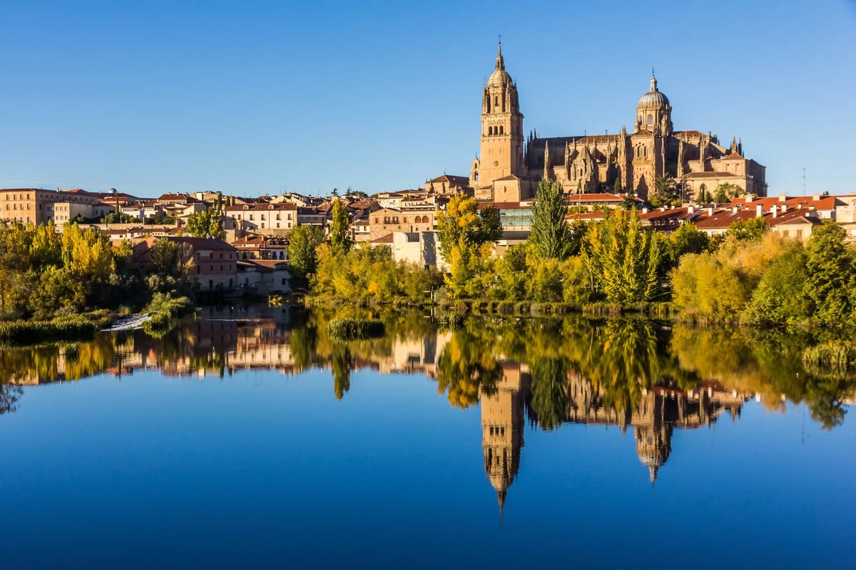 Die monumentale Silhouette Salamancas mit ihrer berühmten Kathedrale spiegelt sich eindrucksvoll im ruhigen Wasser des Flusses Tormes