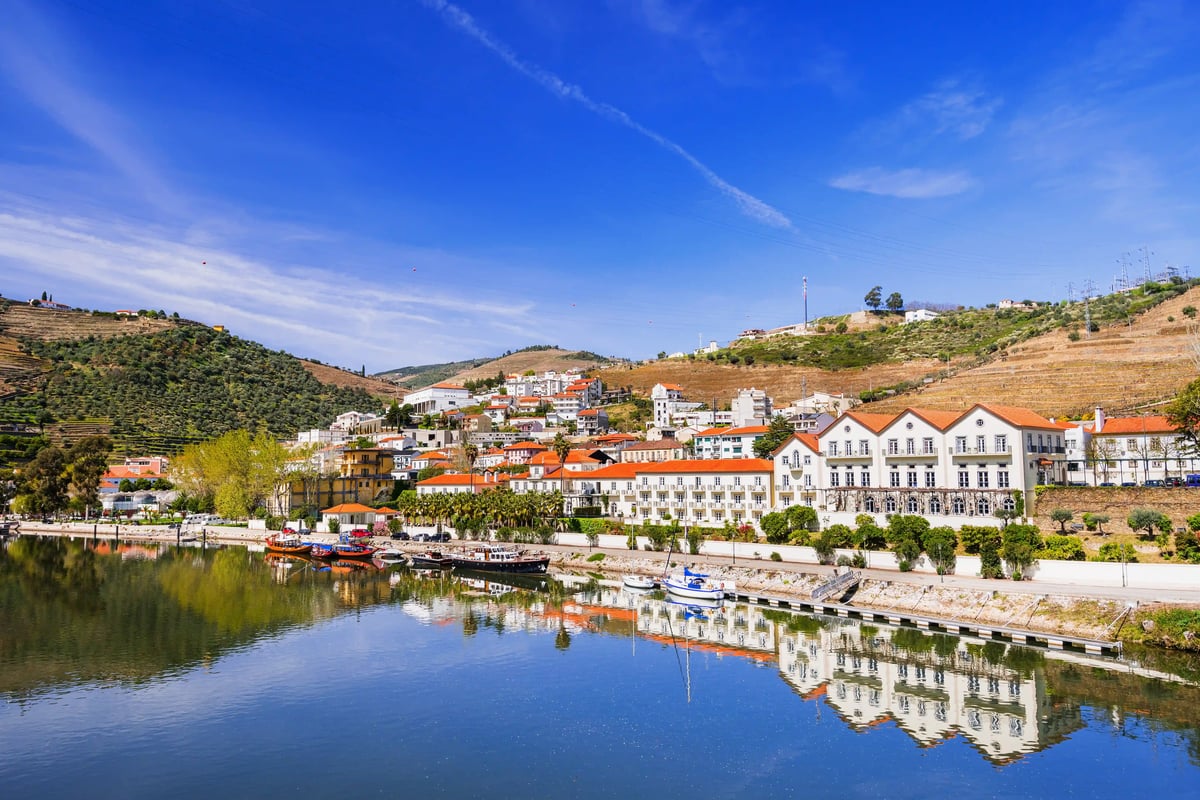 Village de Pinhão au bord du Douro avec maisons riveraines, bateaux et vignobles verdoyants sur les coteaux