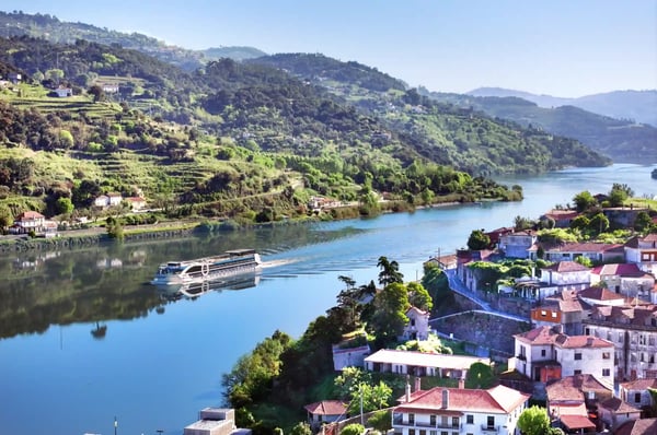 Flussschiff fährt auf dem Douro durch grüne Hügellandschaft mit Weinbergen und kleinen Ortschaften