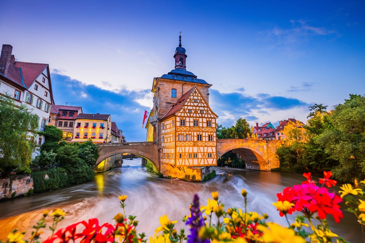 Historisches Rathaus mit Fachwerk über einem Fluss und Steinbrücke bei Abendlicht