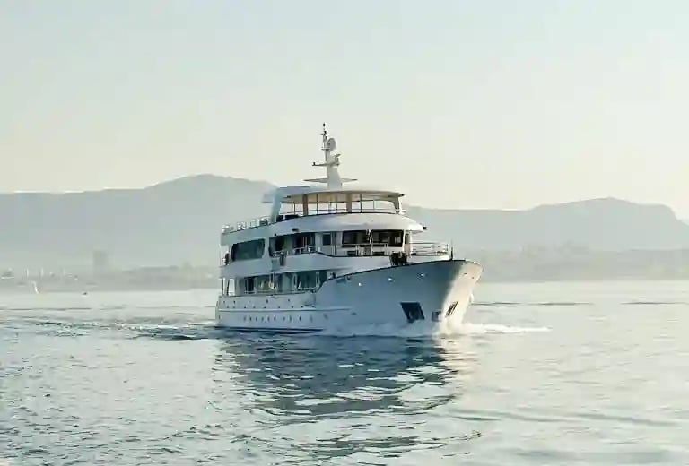 Kleines Kreuzfahrtschiff auf ruhiger Adria vor einer Küstenlandschaft im Morgenlicht.