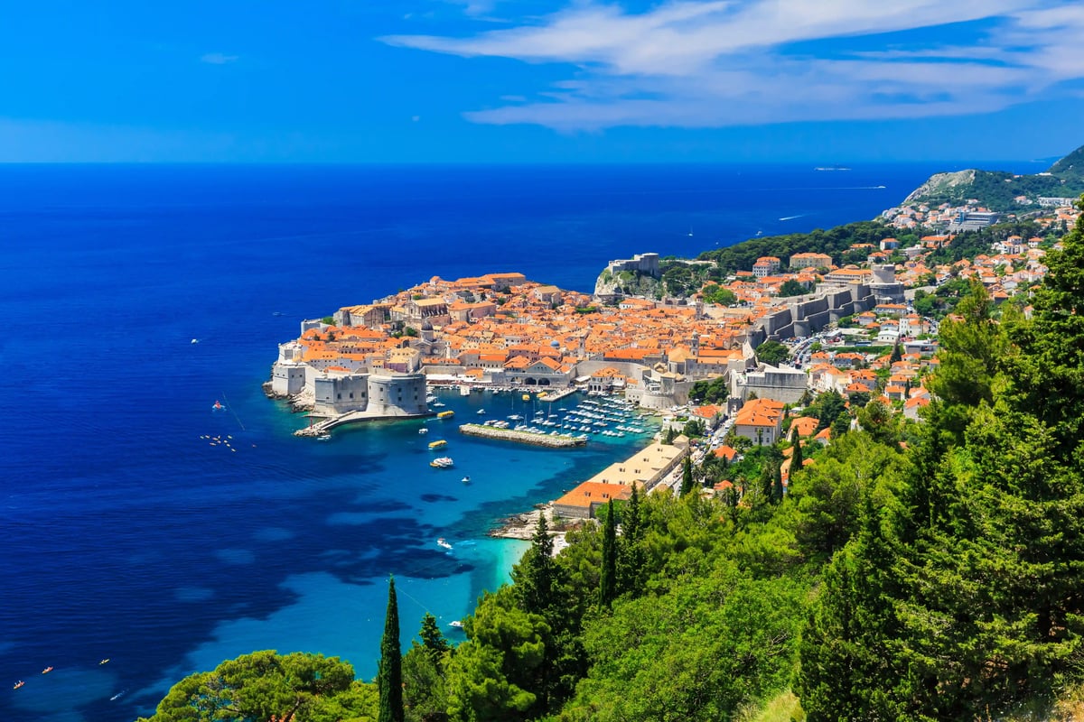 Panoramablick auf Dubrovnik mit orangefarbenen Dächern, Hafen und tiefblauem Meer aus erhöhter Perspektive