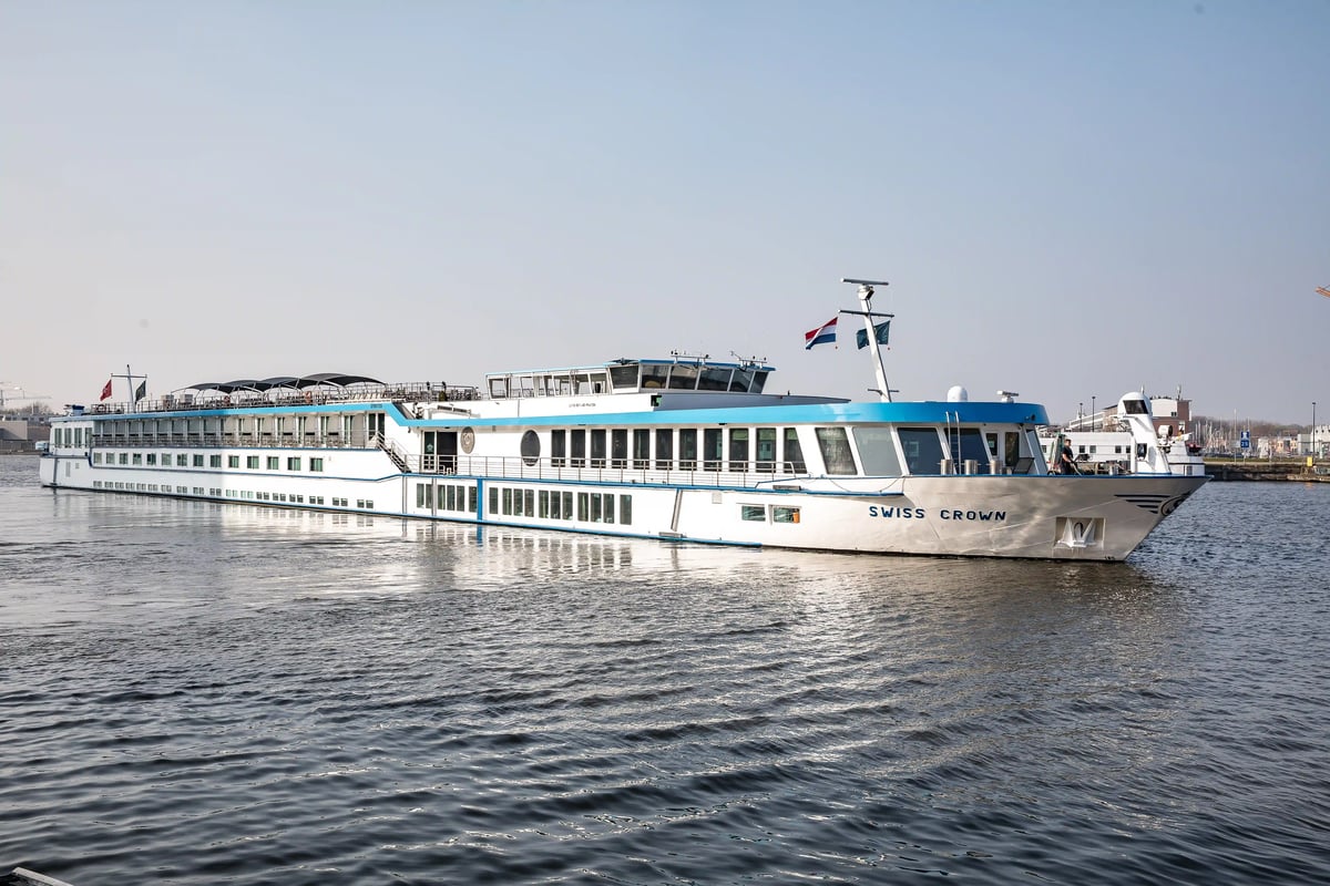 Flusskreuzfahrtschiff Swiss Crown fährt auf dem Rhein bei ruhigem Wasser und hellem Himmel
