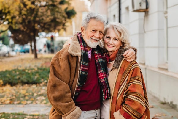 Älteres Paar umarmt sich lächelnd bei einem Spaziergang im herbstlichen Stadtpark