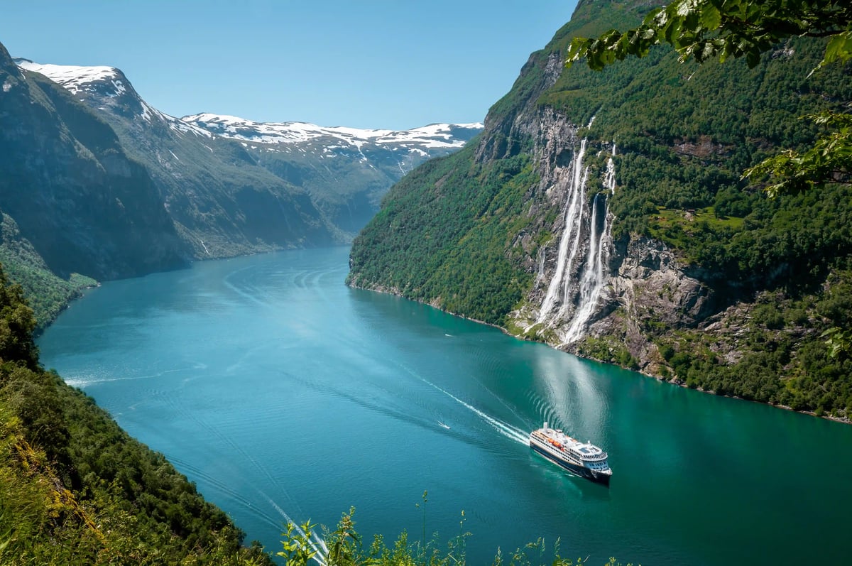 Kreuzfahrtschiff fährt durch Fjord mit steilen Felswänden