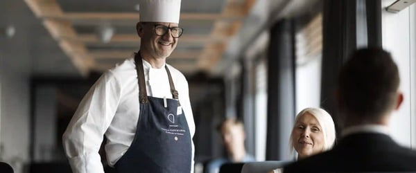 Koch im Bordrestaurant eines Kreuzfahrtschiffes begruesst Gäste in heller moderner Umgebung