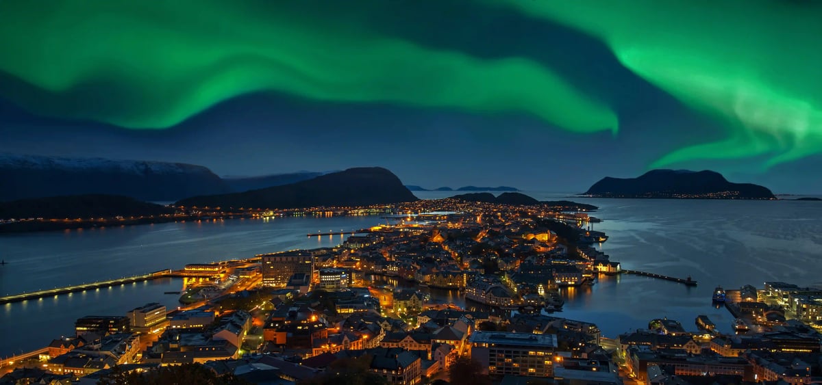 ne vue aérienne nocturne de la ville d'Ålesund en Norvège sous une aurore boréale verte éclatante dans le ciel sombre.