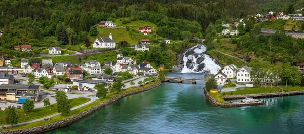 Blick auf Hellesylt mit Wasserfall, kleinen Häusern und grüner Fjordlandschaft