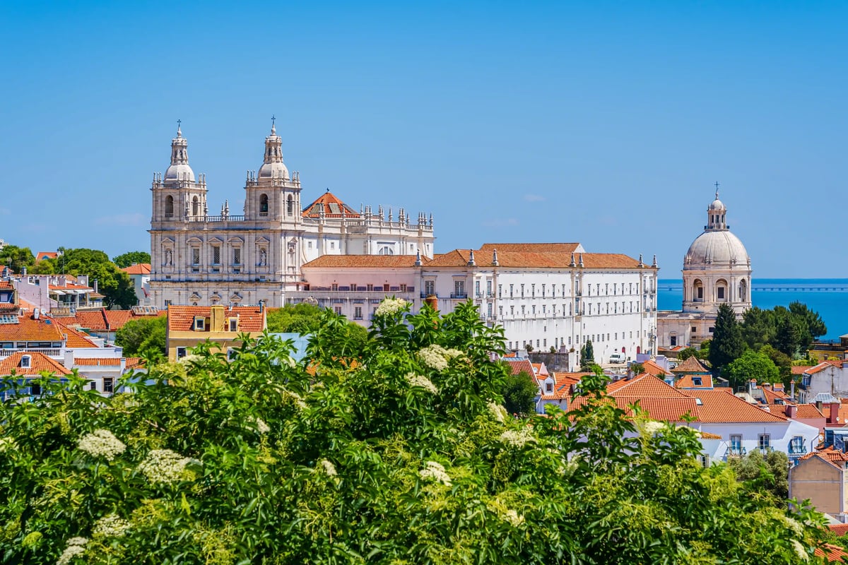 Blick auf die farbenfrohen Häuser von Lissabon mit Burg auf dem Hügel und Brücke im Hintergrund bei warmem Abendlicht