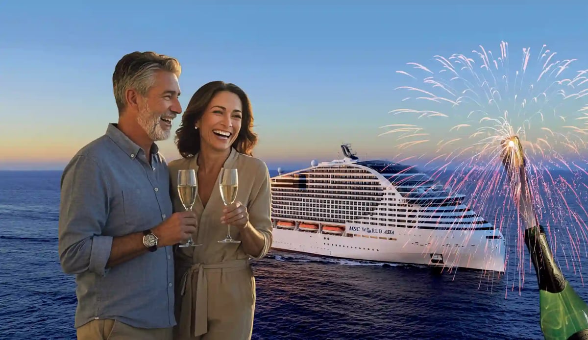 Paar mit Sektgläsern vor der MSC World Asia auf See, waehrend ein Feuerwerk den Abendhimmel erleuchtet.