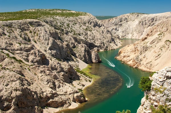 Tiefer Felscanyon mit gruengrünem Fluss und Boot im Zrmanja Canyon