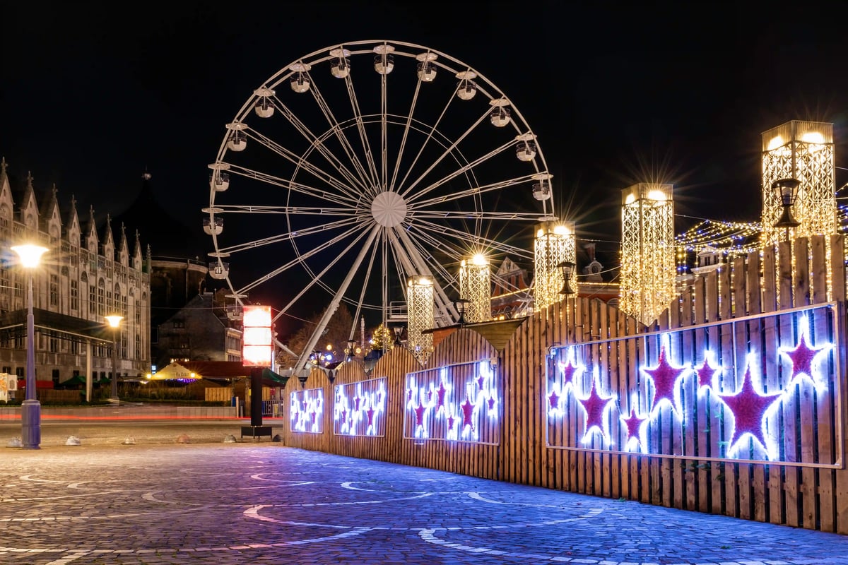 Marché de Noël illuminé avec grande roue et décorations lumineuses de nuit sur une place urbaine