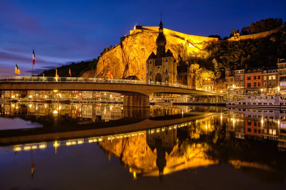 Vue nocturne de Dinant avec citadelle illuminée, église et pont le long de la Meuse