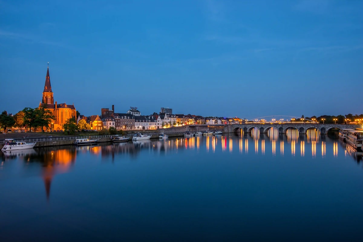 Vue du soir de la Meuse avec pont historique, lumières de la ville et reflets dans l'eau