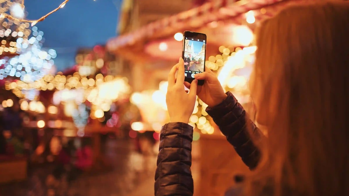 Personne photographiant un marché de Noël illuminé avec un smartphone en soirée