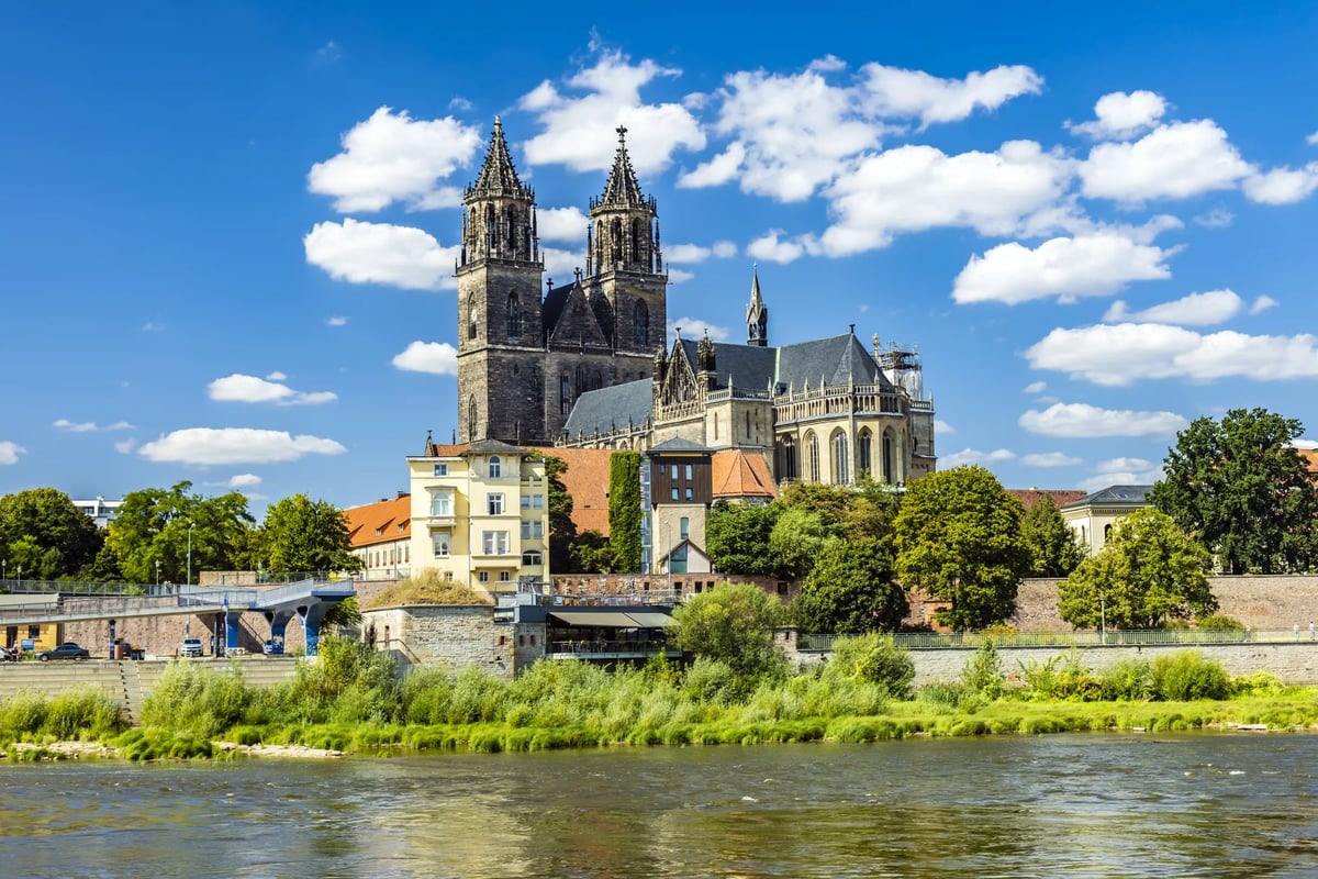 Blick über die Elbe auf den Magdeburger Dom mit seinen markanten Doppeltürmen unter blauem Himmel mit weißen Wolken