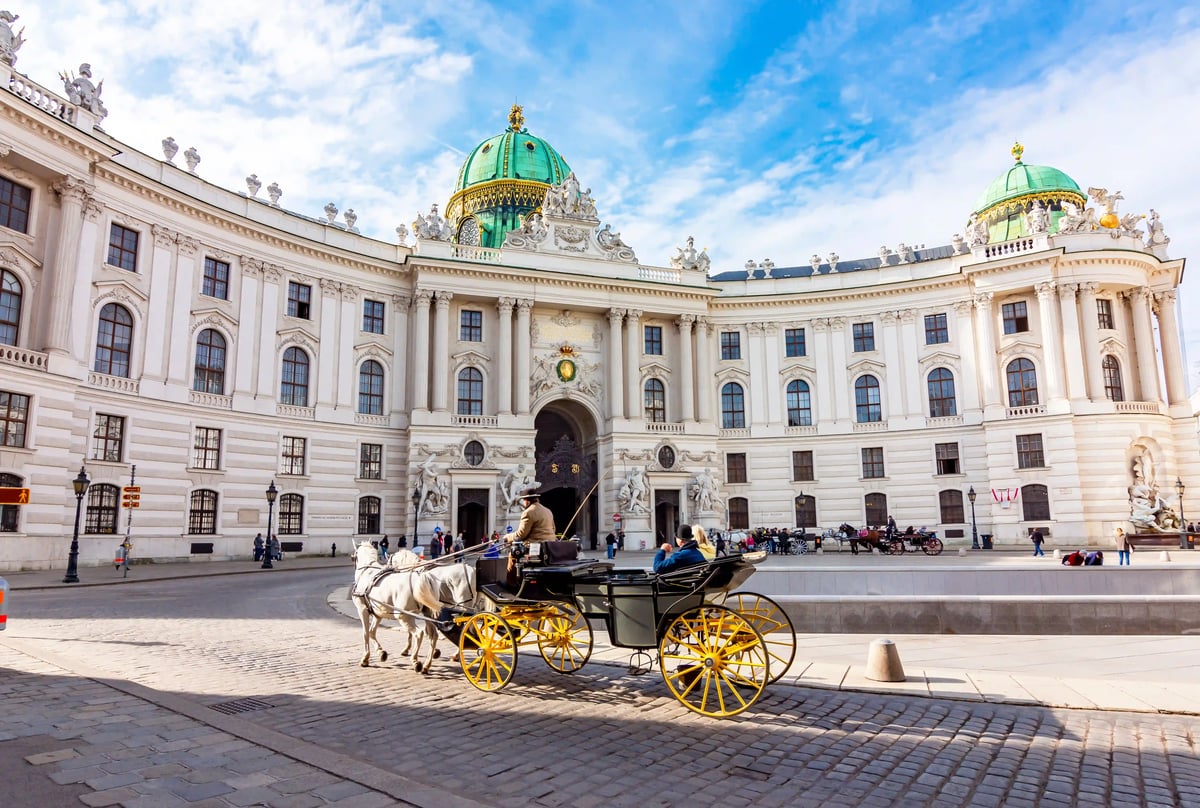 Vor der Hofburg Wien wartet eine Pferdekutsche auf dem Platz, Menschen gehen vorbei