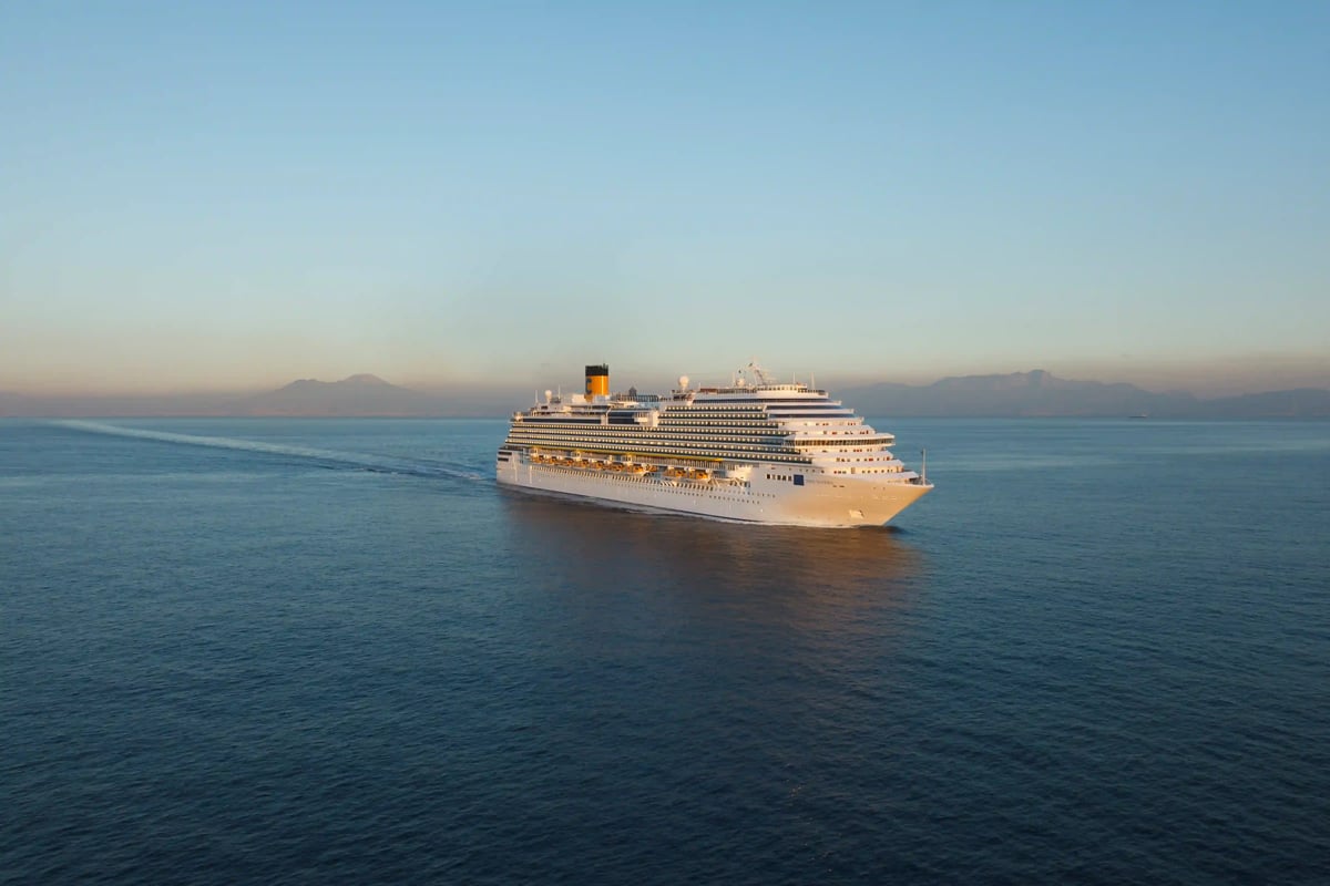 Grosses Kreuzfahrtschiff fährt bei ruhigem Meer und klarem Himmel entlang einer Kueste in der Abendstimmung