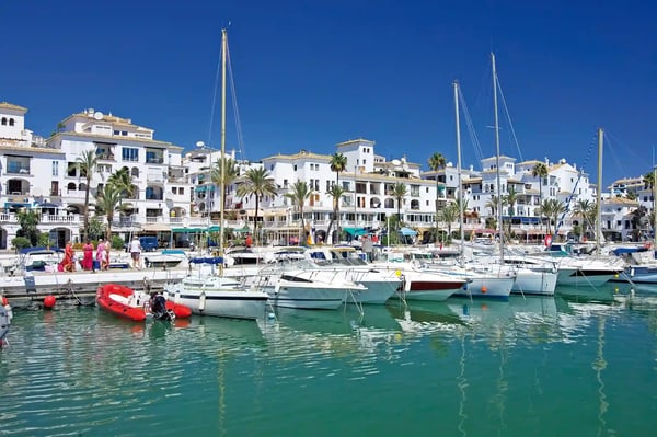 Yachthafen in Málaga mit weissen Booten, Palmen und Wohnhäusern bei sonnigem Himmel