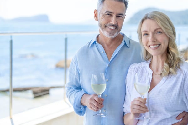 Lächelndes Paar hält Weingläser auf dem Deck eines Kreuzfahrtschiffes mit Meerblick