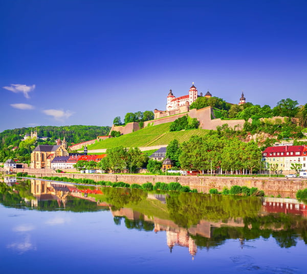 Festung Marienberg thront über Würzburg; darunter spiegeln sich Ufer und Altstadt im ruhigen Fluss.