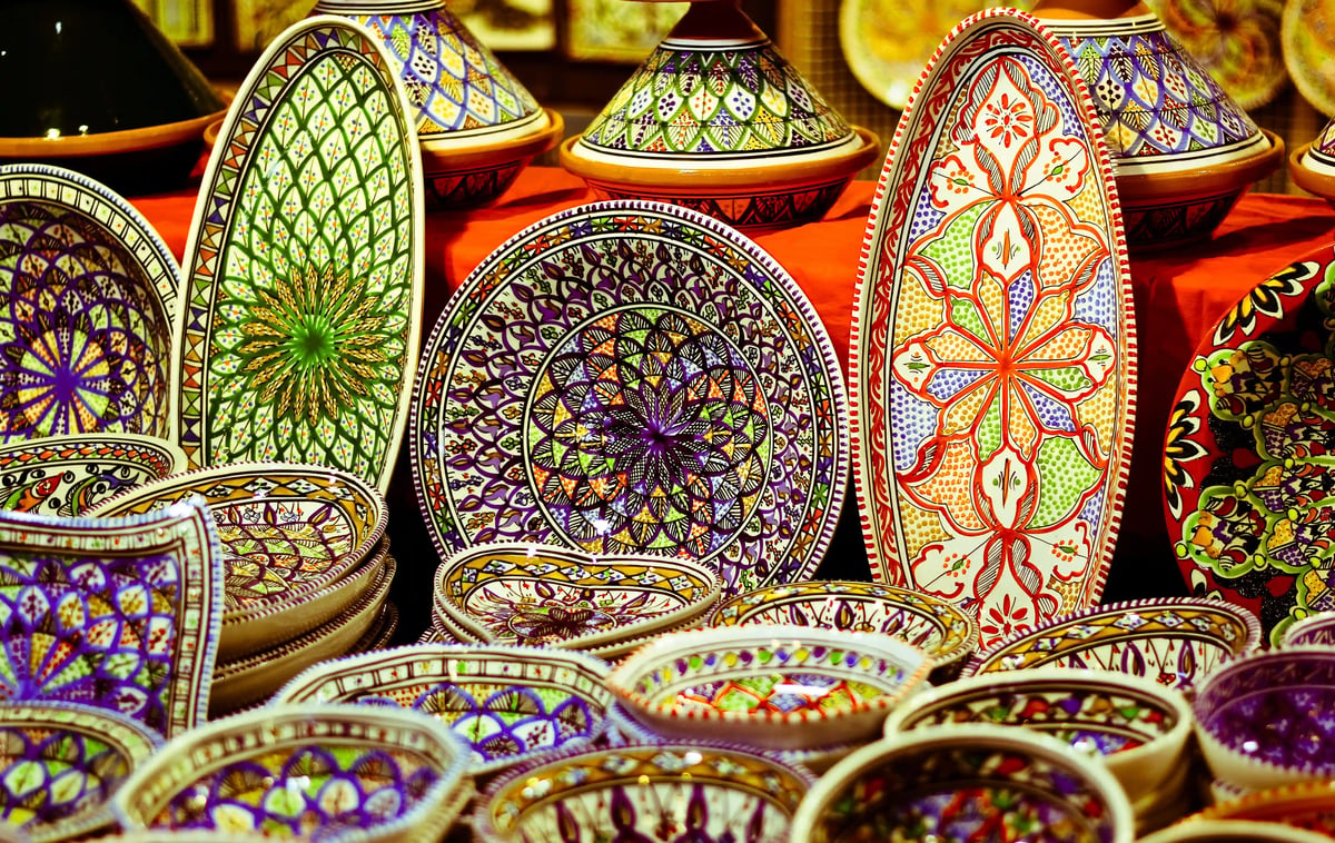 Farbenfrohe handbemalte Keramikschalen und Tajine auf einem orientalischen Markt mit kunstvollen Mustern und leuchtenden Farben
