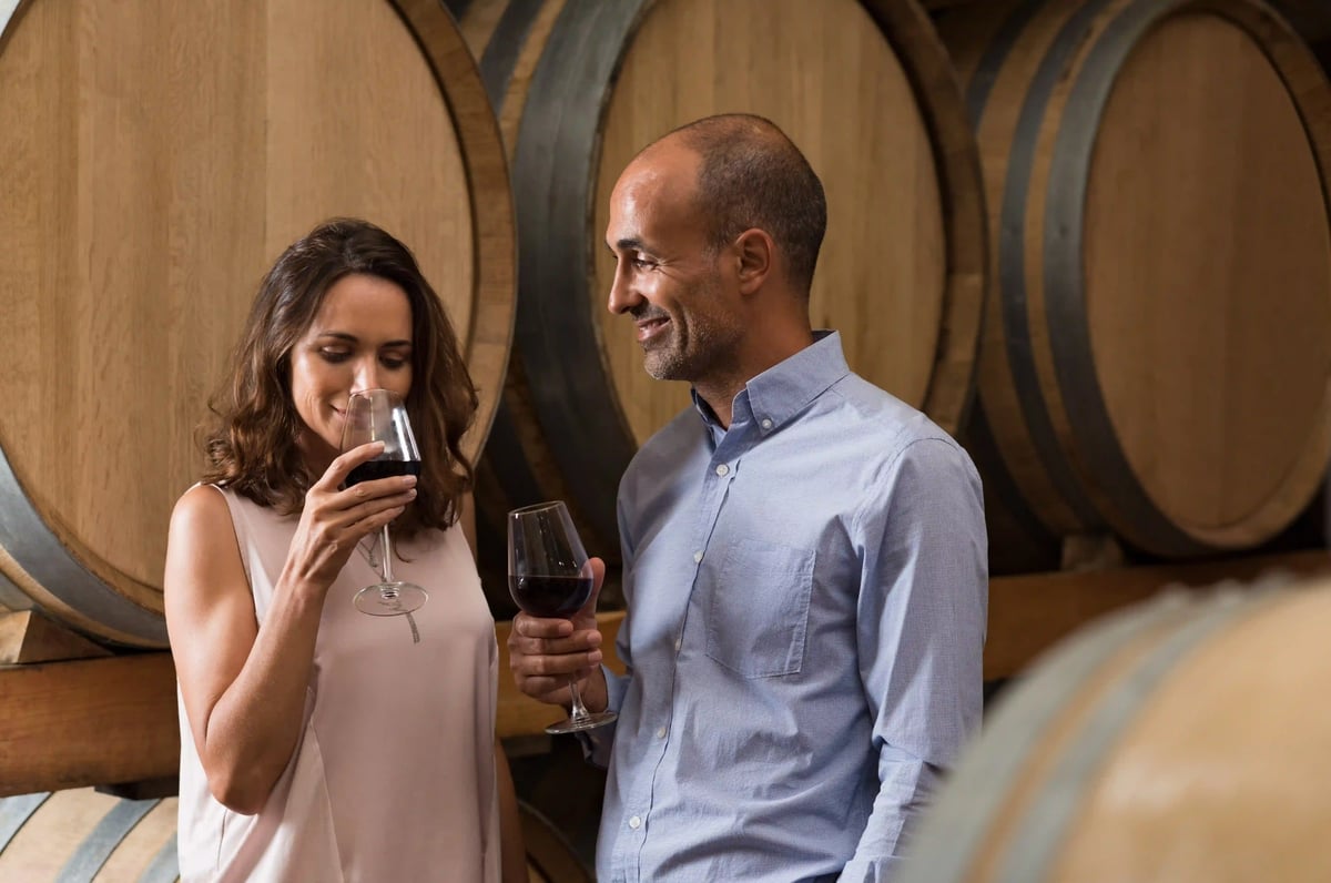 Couple dégustant du vin dans une cave de la région de la Moselle, entouré de grands fûts en bois et de verres de vin rouge