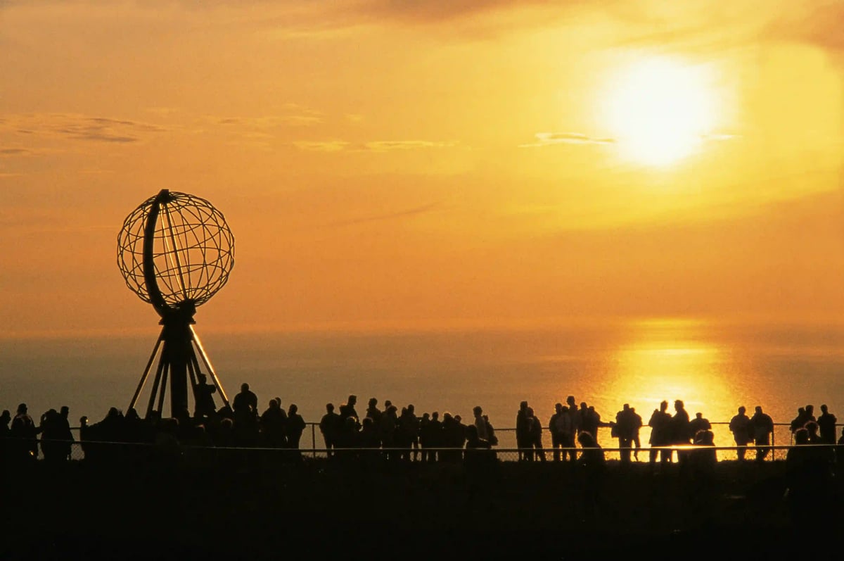 Soleil de minuit au cap Nord avec silhouettes de personnes et mer doree