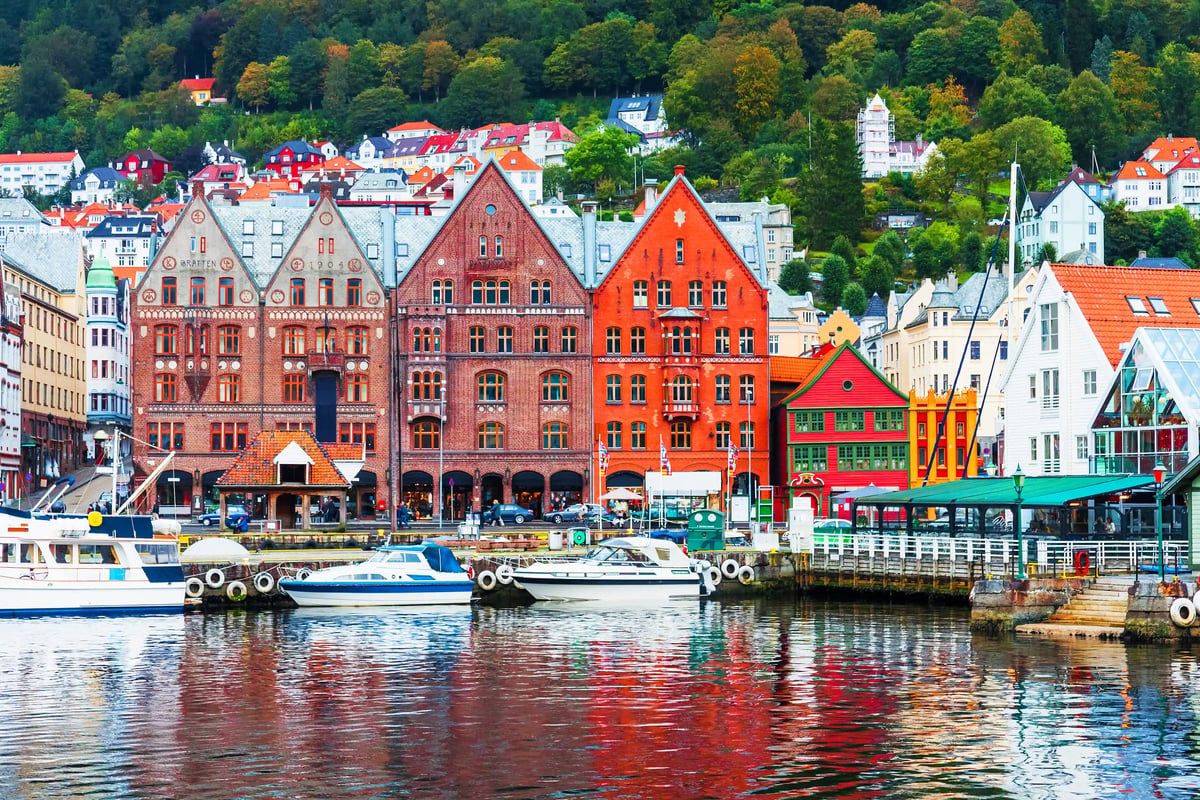 Maisons historiques colorées à pignons le long du port de Bergen avec bateaux et collines boisées en arrière plan