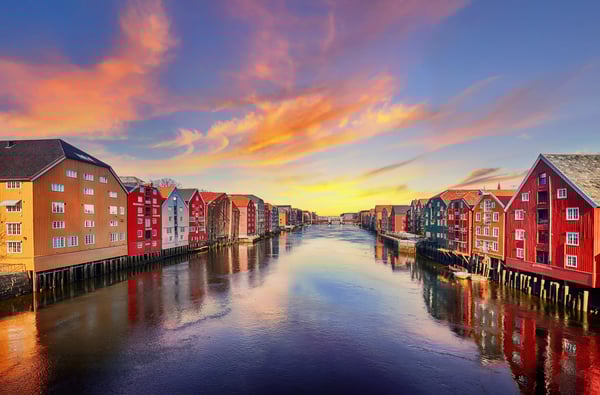 Bunte historische Speicherhäuser entlang des Flusses in Trondheim mit Spiegelungen im Wasser bei Sonnenuntergang