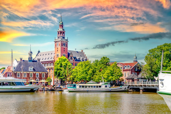 Historische Hafenstadt in Ostfriesland mit Backsteinbauten, Schiffen und Kirchturm am Wasser.