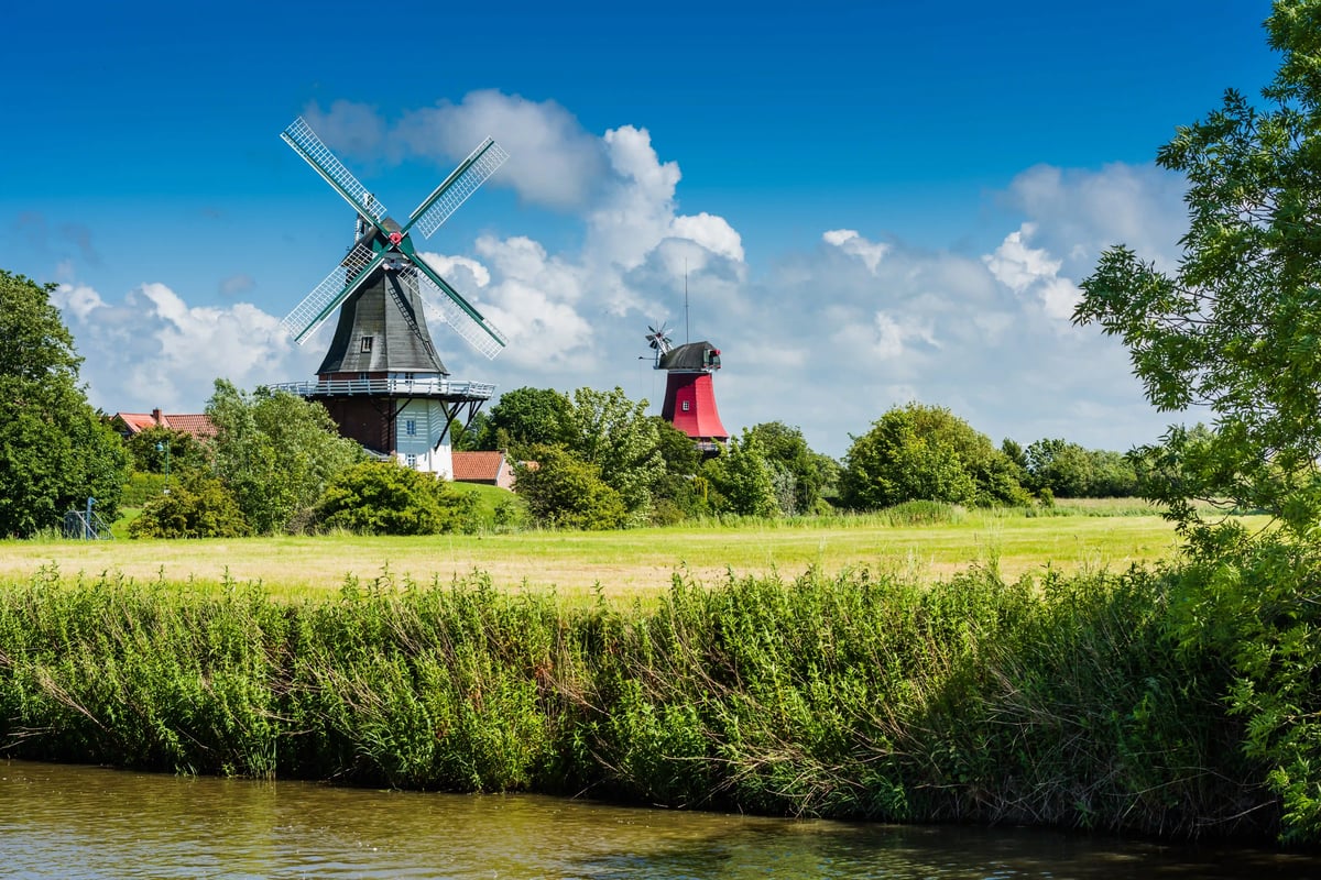 Historische Windmühlen und grüne Wiesen entlang eines Kanals in Ostfriesland