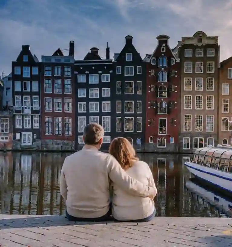 Zwei Personen sitzen am Kanal von Amsterdam vor einer Reihe historischer Grachtenhäuser