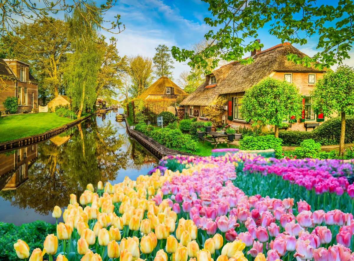 Blumenbeete und reetgedeckte Häuser entlang eines ruhigen Kanals in Giethoorn