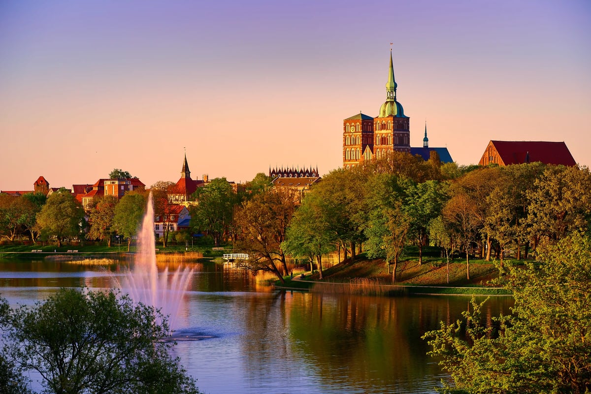 Blick auf Stralsund mit Kirchturm, Parkanlage und See im Abendlicht