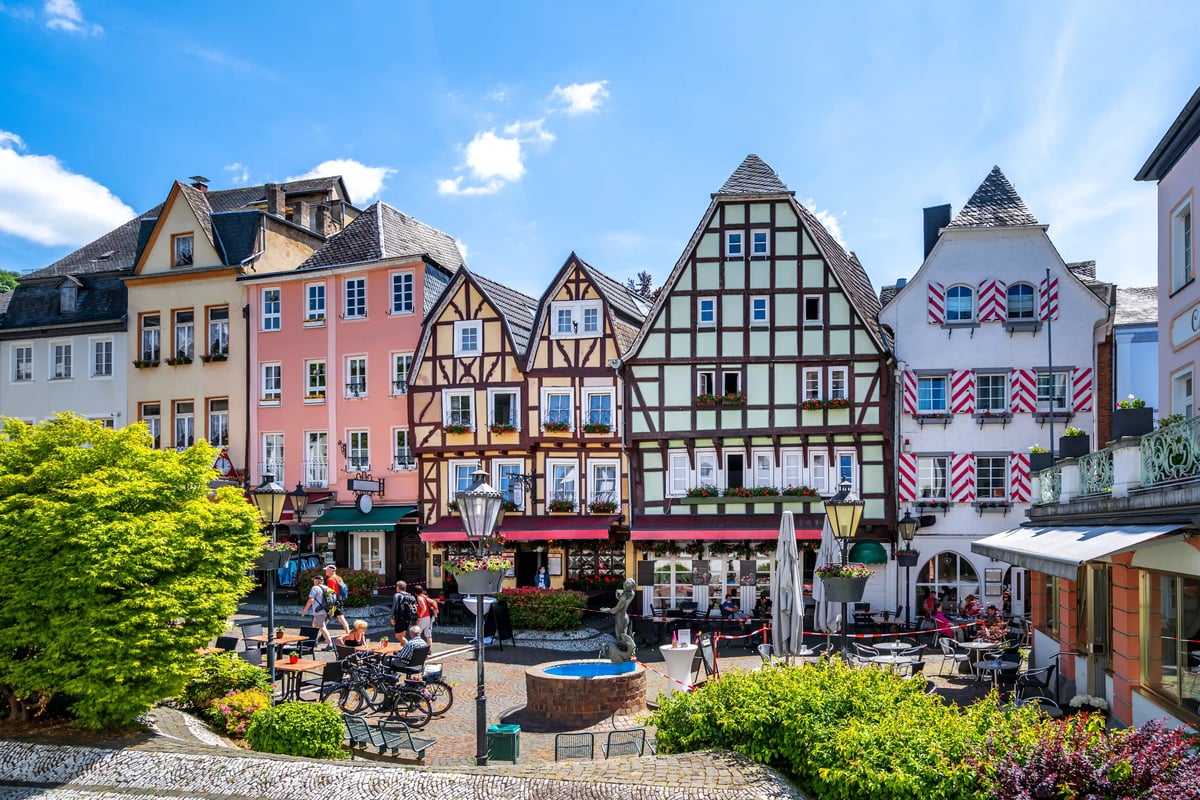 Historischer Marktplatz in Linz am Rhein mit bunten Fachwerkhäusern, Brunnen und Sitzgelegenheiten unter blauem Himmel.