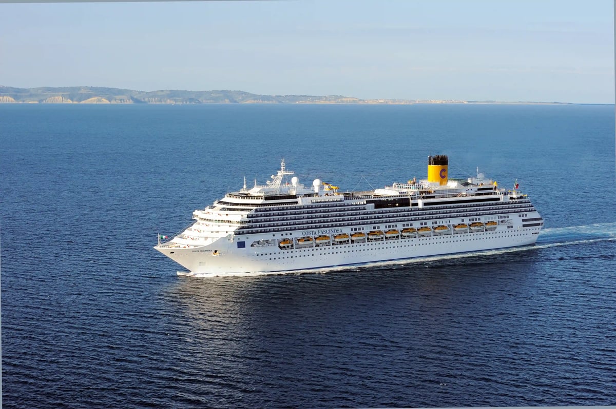 Grosses Kreuzfahrtschiff Costa Fascinosa fährt bei ruhiger See im Mittelmeer, im Hintergrund eine ferne Kuestenlandschaft
