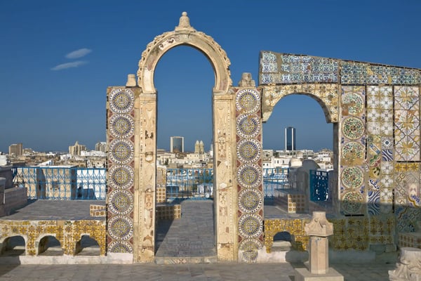 Verzierte Steinbögen mit bunten Mosaiken in der Medina von Tunis, Stadtansicht im Hintergrund