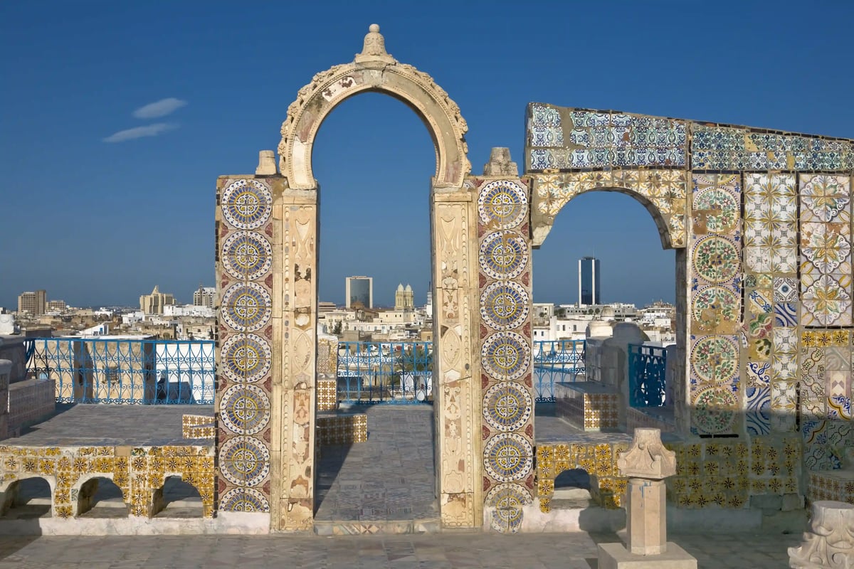 Des arcs en pierre ornés de mosaïques colorées dans la médina de Tunis, avec une vue sur la ville en arrière-plan
