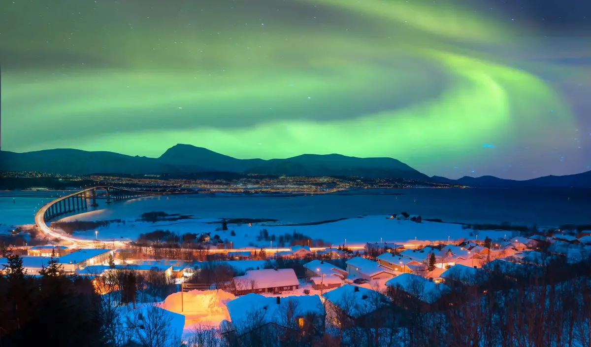 Nordlichter über der verschneiten Landschaft und der beleuchteten Küste bei Tromsø.