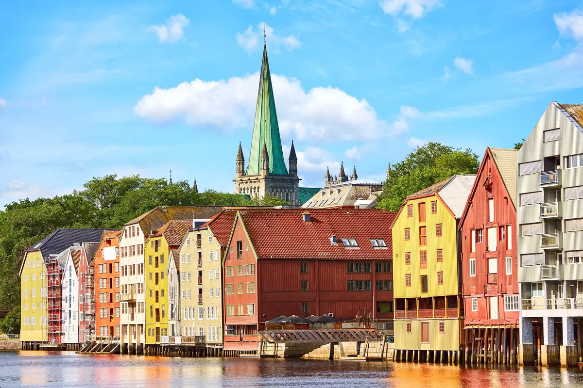 Bunte Speicherhäuser am Wasser mit dem Nidarosdom im Hintergrund in Trondheim.