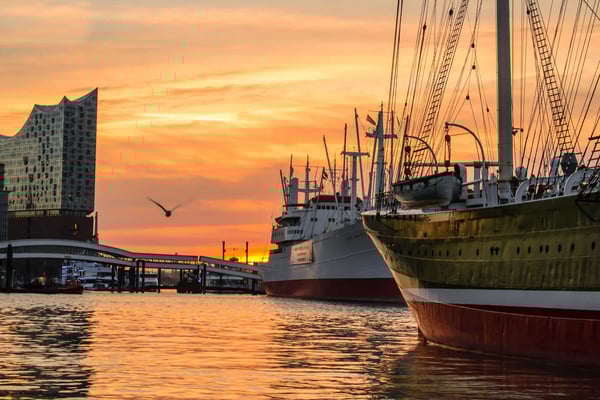 Historische Schiffe liegen im Hamburger Hafen vor orangefarbenem Sonnenuntergang mit Blick auf die Elbphilharmonie