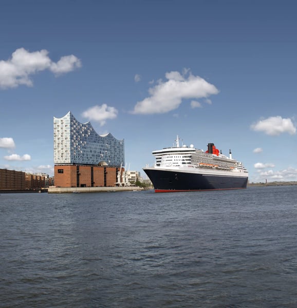 Kreuzfahrtschiff Queen Mary 2 liegt auf der Elbe vor der Hamburger Elbphilharmonie bei Tageslicht