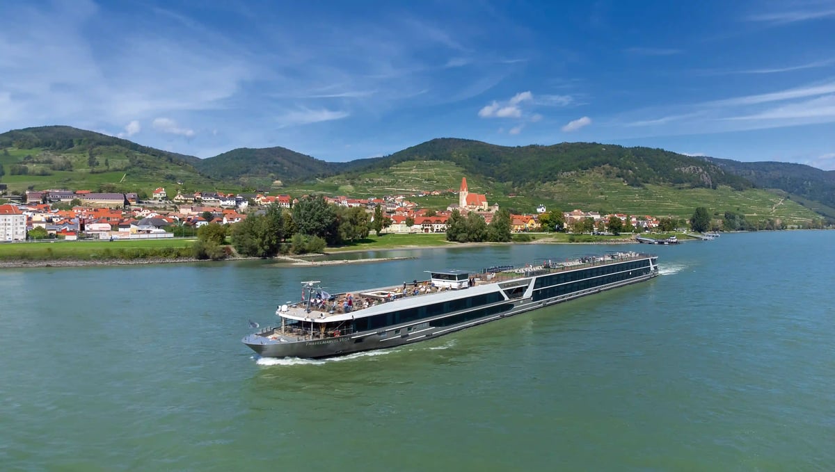 Modernes Flusskreuzfahrtschiff fährt auf dem Rhein vorbei an Weinbergen und einer Ortschaft