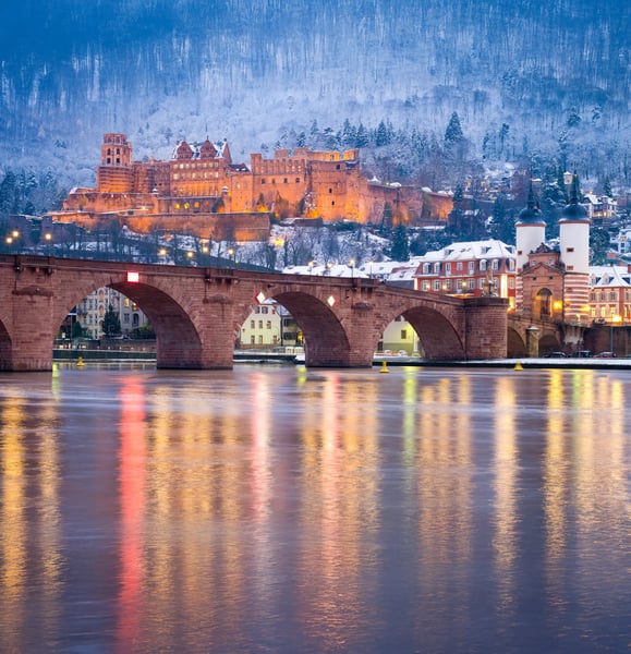 Winterlicher Blick auf das Schloss Heidelberg mit verschneiten Hängen und beleuchteter Altstadt