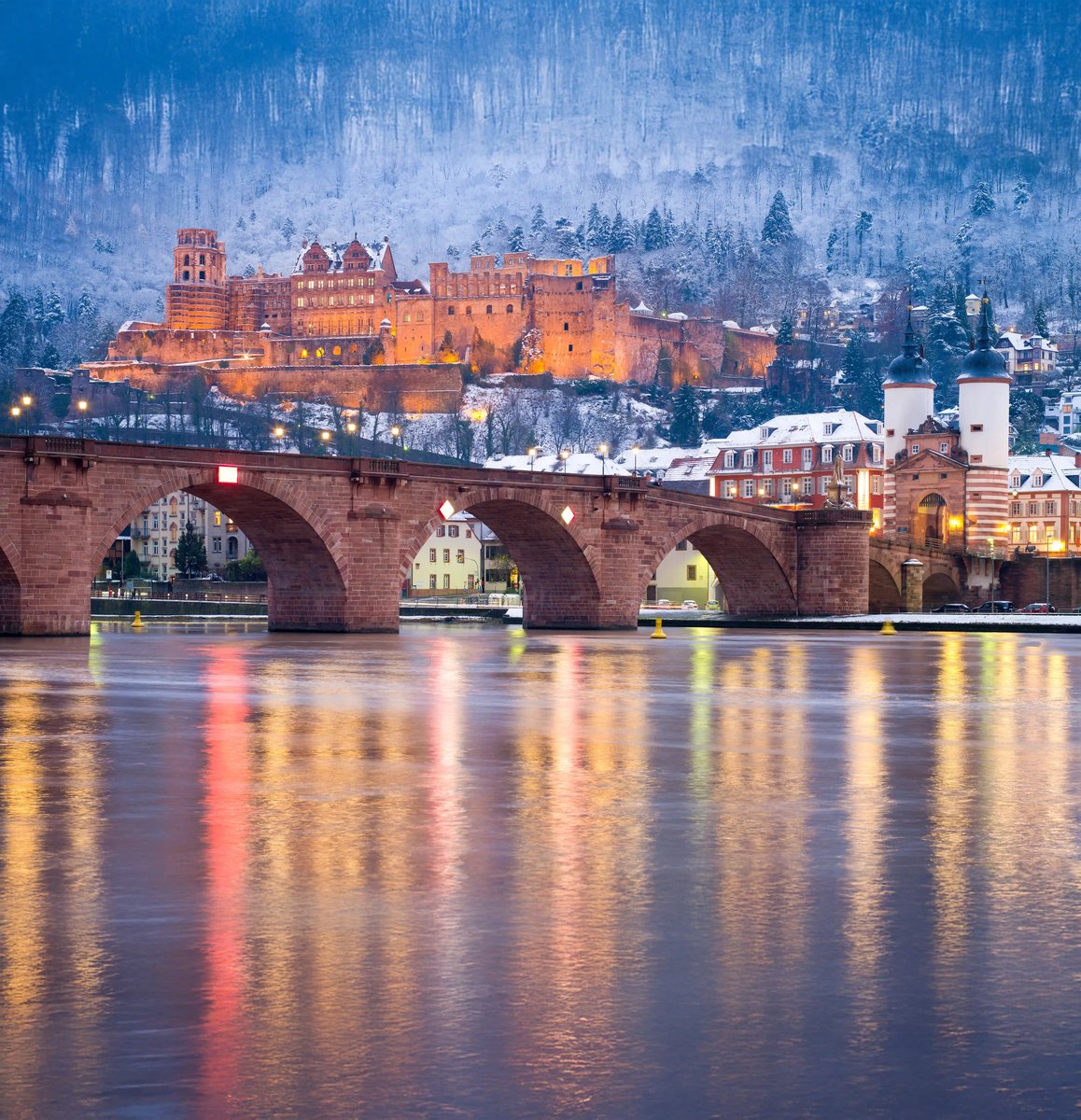 Winterlicher Blick auf das Schloss Heidelberg mit verschneiten Hängen und beleuchteter Altstadt